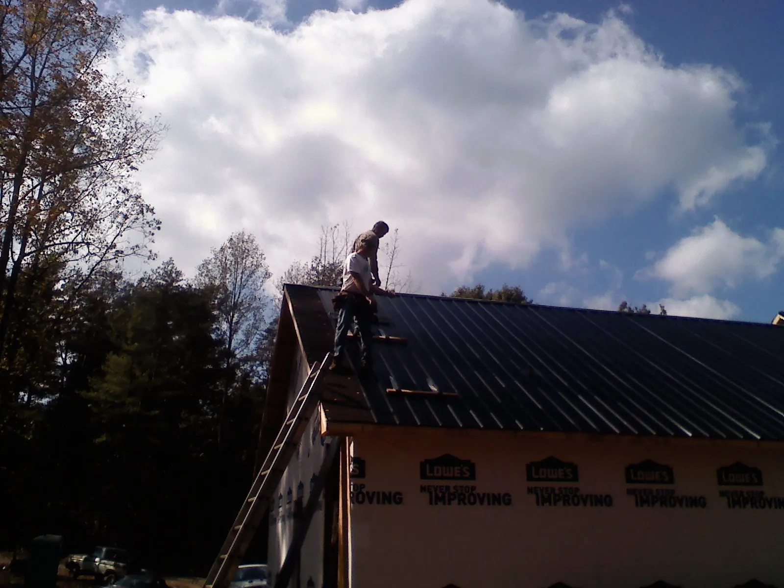 Roofer fastening dark metal panels high against a cloudy sky, from a Roof Inspection job in Maurice